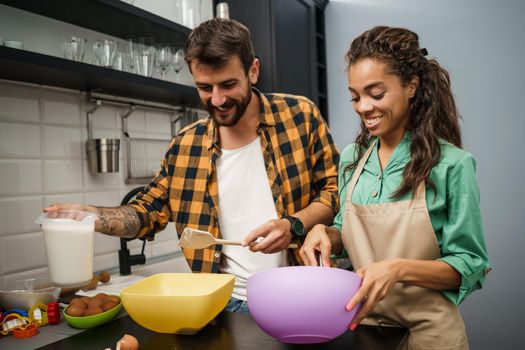 Happy multiethnic couple cooking in their kitchen. They are making cookies.