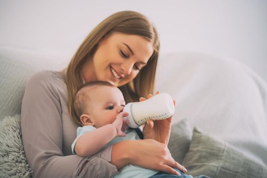 Happy mother is feeding her baby boy at home.