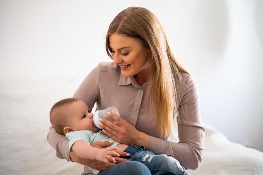 Happy mother is feeding her baby boy at home.