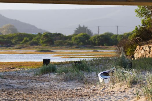 Small rowing boat stranded on a sandy coastal riverbank, Mossel Bay, South Africa