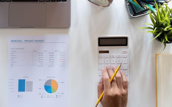 Top view hand of accountant using calculator on workplace with copy space, calculator and plant potted on white desk background, Accounting workplace concept.