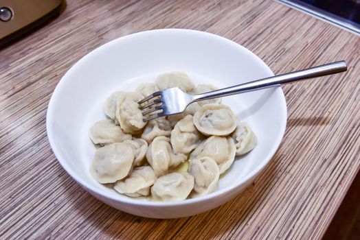 plate with homemade Russian dumplings on a wooden table and a fork in the plate.