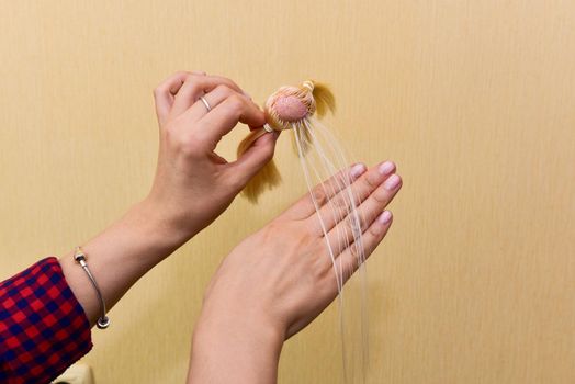 female hands and holding a doll head, how to make a doll hairstyle, hobby concept.