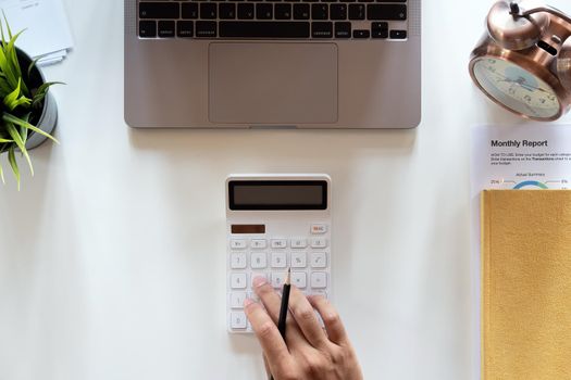 Top view hand of accountant using calculator on workplace with copy space, calculator and plant potted on white desk background, Accounting workplace concept.