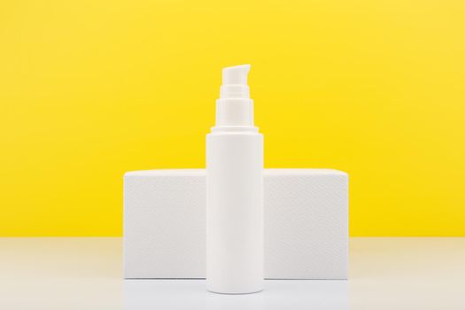 Face moisturizing cream or lotion in tall white tube against white geometric podium and yellow background with copy space. Concept of skin moisturizing and protective treatment with Spf for summer