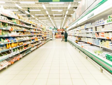 Abstract blurred supermarket aisle with colorful shelves and unrecognizable customers as background