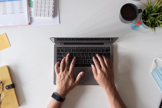 Top view of male hands working on modern laptop calculator financial report and medical face mask on white background, business accounting with new normal during Covid 19 pandemic concept