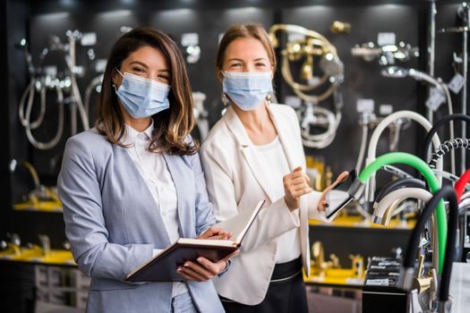 Businesswoman owning small business bath store. She is talking with a customer who is choosing the goods. They are wearing protective face mask.
