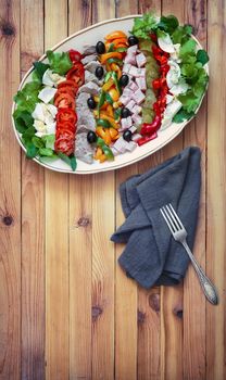 A popular dish of American cuisine - Cobb salad, consisting of greens, eggs, tomatoes, cheese, meat products, stacked in rows on a wide dish and poured sauce.