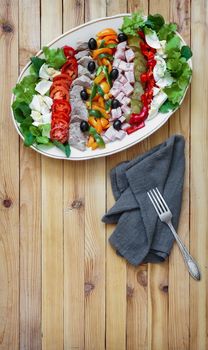 A popular dish of American cuisine - Cobb salad, consisting of greens, eggs, tomatoes, cheese, meat products, stacked in rows on a wide dish and poured sauce.