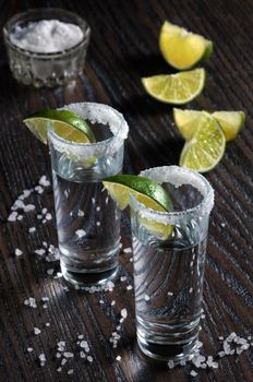Portion of tequila, framed with a salt edge with slice lime in tall shot glasses