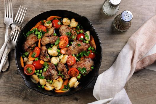Fried chicken liver with vegetable side dish of tomatoes, carrots, mushrooms, peas in a pan