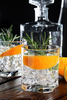 Cocktail classic Dry Gin with tonic and orange zest with a sprig of rosemary on a wooden board with  slices   juicy orange
