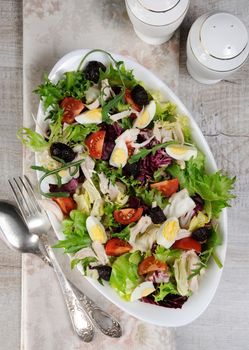 Light salad from the mix of lettuce leaves with tomatoes, eggs, slices of chicken breast and dried olives