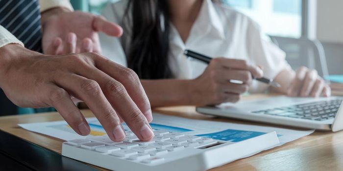 Close up of businessman or accountant hand holding pen working on calculator to calculate business data, accountancy document and laptop computer at office, business concept.