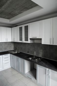 Modern minimalism style kitchen interior in monochrome tones. Custom kitchen with grey white facadesmdf and dark grey countertop with installed kitchen hood and sink. Modular kitchen from chipboard