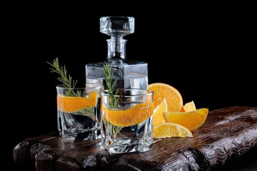 Cocktail classic Dry Gin with tonic and orange zest with a sprig of rosemary on a wooden board with  slices   juicy orange