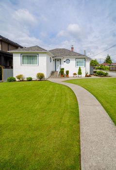 Main entrance of small residential house with concrete walkway over green lawn of front yard. Family house with doorsteps to the entrance