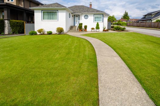 Main entrance of small residential house with concrete walkway over green lawn of front yard. Family house with doorsteps to the entrance