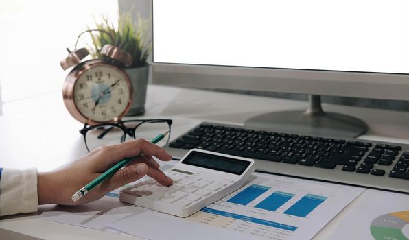 Close up of businessman or accountant hand holding pen working on calculator to calculate business data, accountancy document and laptop computer at office, business concept.