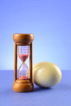 A kitchen egg timer with a hard boiled egg over a blue background.