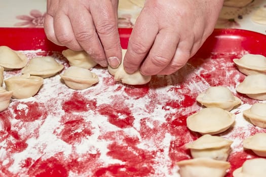 A hand is placing raw dumplings on a red floured tray. Cooking at home