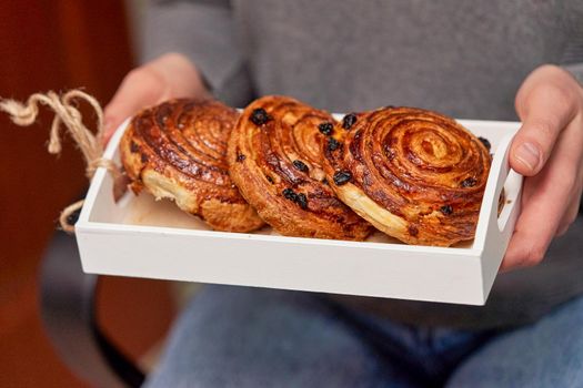 White wooden box with buns with raisins in female hands