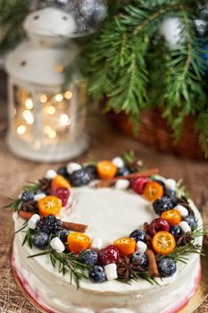 A large round cake decorated with fruits on a Christmas table with a lantern and a spruce branch. Vertical frame