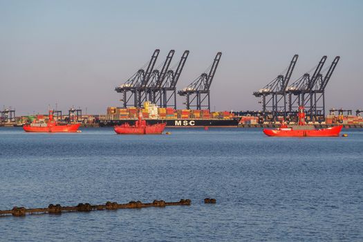 Shotley Point, Suffolk, UK, April 12 2021: Three red lightships moored at mouth of Orwell and Stour estuaries between Port of Felixstowe and Harwich International Port with MSC ship in the background