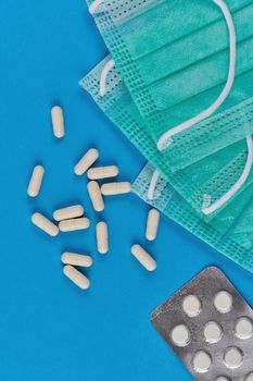 Medical masks, white capsules and pills in packaging on a blue background. Top view, vertical shot