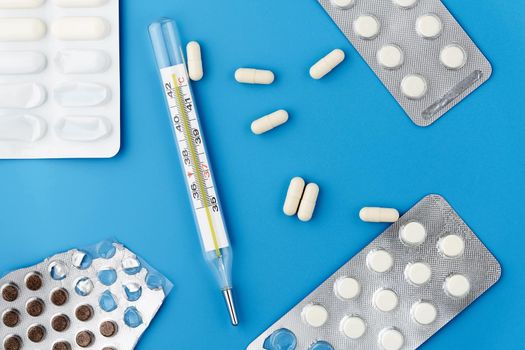 Mercury thermometer, white capsules and tablets in a package on a blue background. View from above