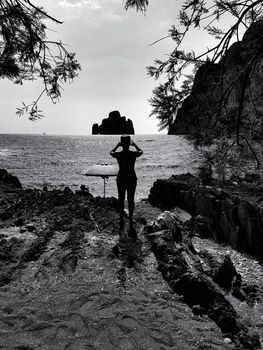 The silhouette of a young woman photographing the sea and an islet from the beach