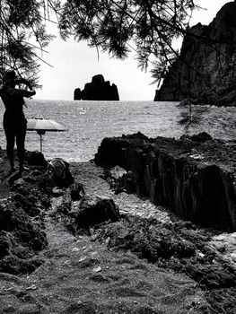 The silhouette of a young woman photographing the sea and an islet from the beach