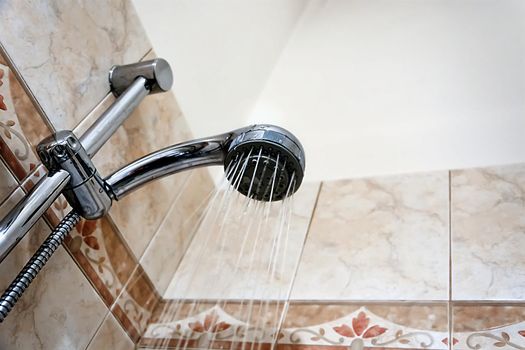 Interior of a shower with water flowing from the shower head. Droplets and moisture. Walls with decorated tiles. Hygiene and personal care