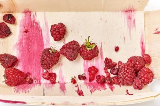 The half-eaten remnants of ripe raspberries in a small wooden container. Top view close up