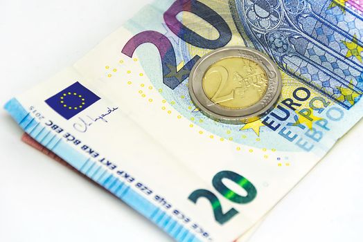 A used 2 euro coin standing on top of a 20 euro banknote. Economics and finance in the European Union.