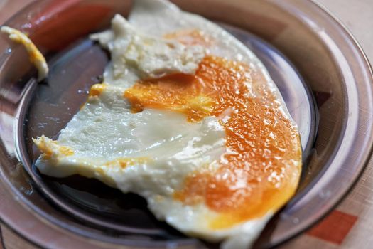 Fried egg with baked yolk in a transparent plate. Morning food.