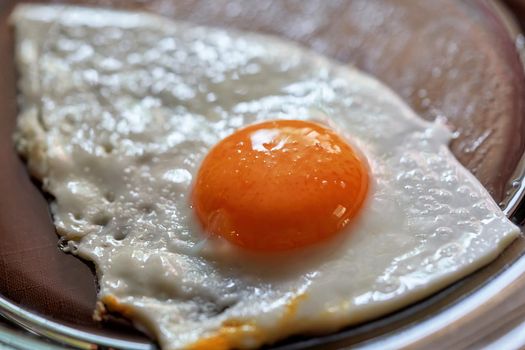Fried egg with a whole round yolk on a transparent glass plate. Tasty breakfast