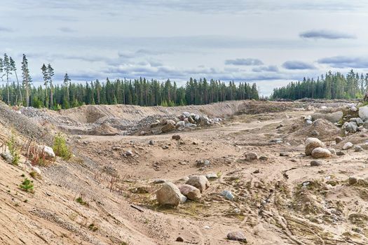 Quarry with sand and large stones against the background of the forest and sky. Sand mining