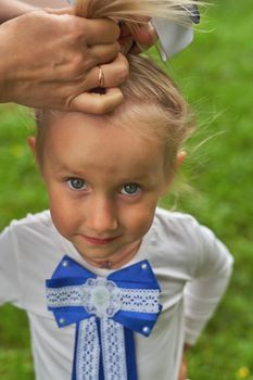 A little girl's hair is combed and a bow is tied. Vertical shot