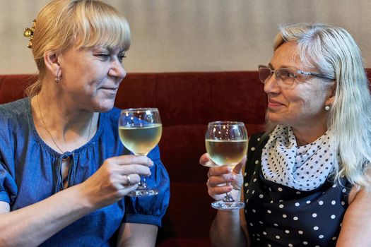 Two elderly blondes with glasses of white wine are sitting in a restaurant. Meeting of two old friends