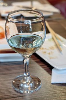 Glass with leftover white wine on table background after meal, vertical frame