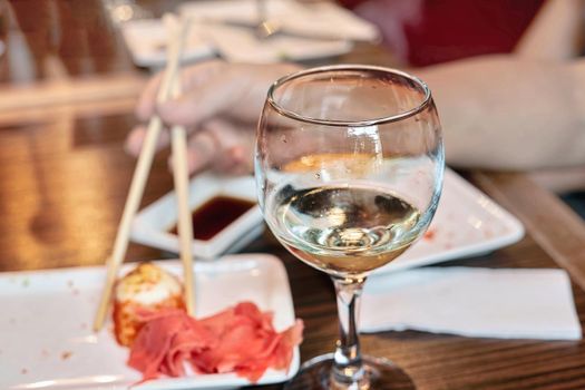 A glass with the remains of white wine on the background of a blurred plate with chopsticks holding sushi