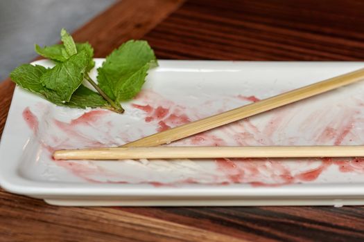 Empty white rectangular plate with wooden chopsticks. Leftover jam and mint leaves