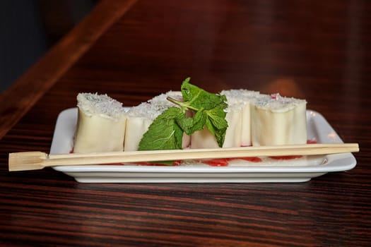 White dish with Japanese minari fruit dessert and green mint leaf and wooden chopsticks