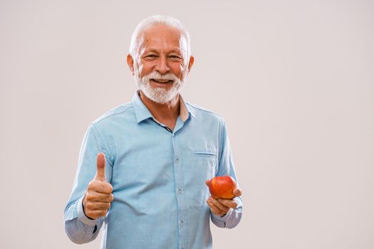 Portrait of cheerful senior man who is holding apple and smiling.