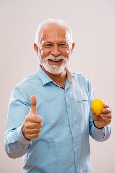 Portrait of cheerful senior man who is holding lemon and smiling.