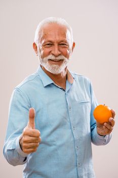 Portrait of cheerful senior man who is holding orange and smiling.