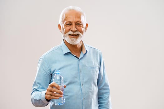 Portrait of cheerful senior man who is holding bottle of water and smiling.