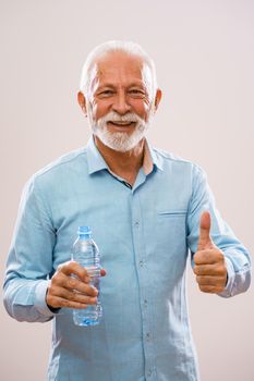 Portrait of cheerful senior man who is holding bottle of water and smiling.